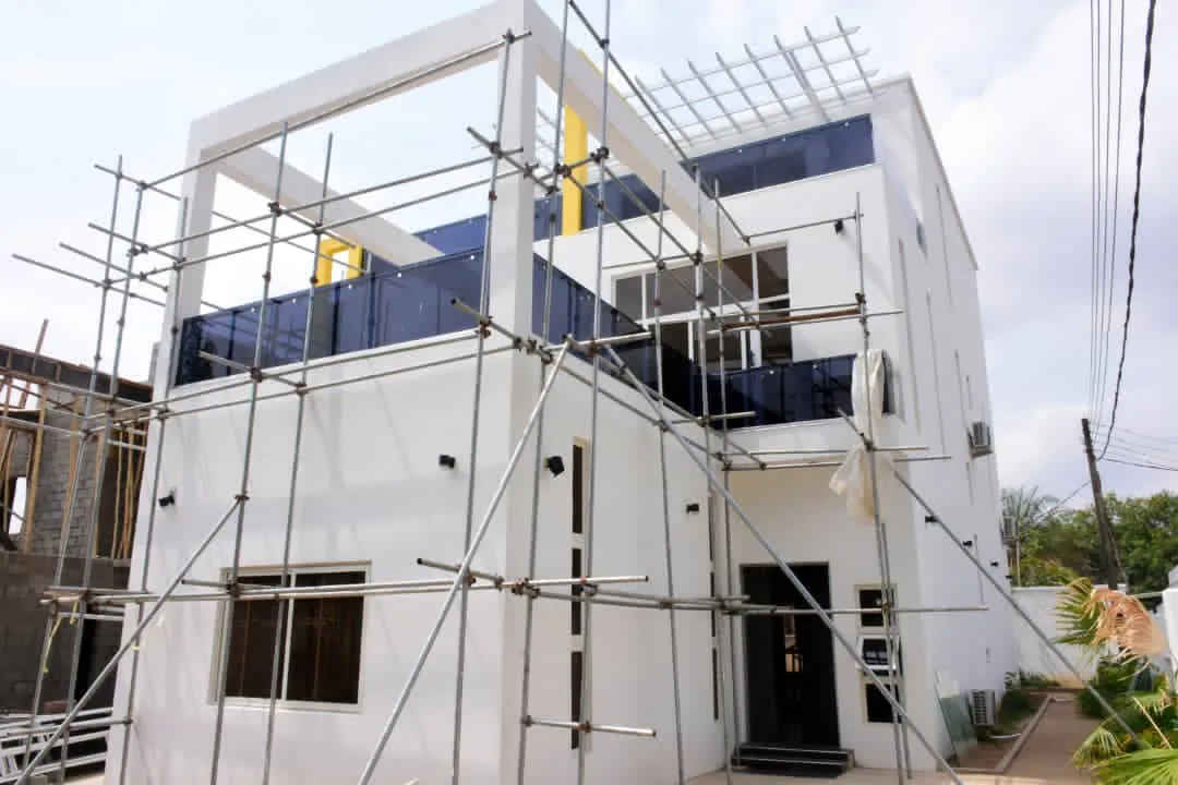 White contemporary townhouse under scaffolding, with glass balconies and a roof pergola